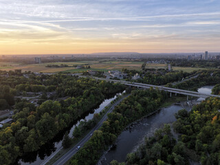 Fototapeta premium Aerial view of a winding river flowing through a forested landscape with a bridge and a distant city on the horizon