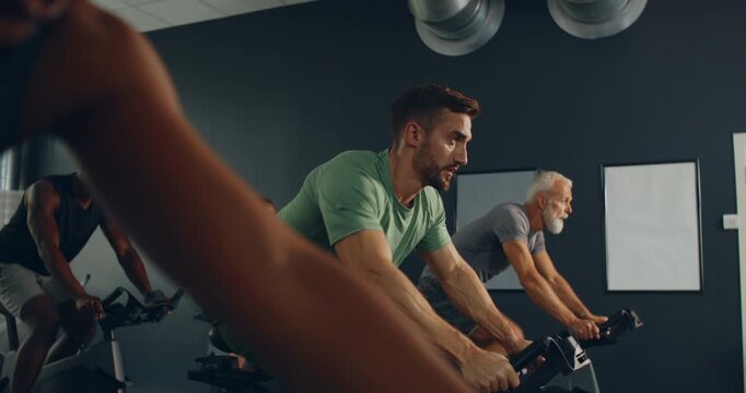 Fit young man in sportswear riding on
a stationary bike during a cycling
class with others in a gym