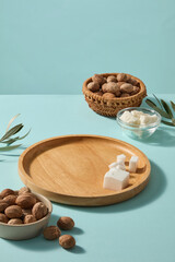 Advertising scene of creamy shea butter, rustic wooden plate and shea nuts scattered softly, leaving airy space for copy in beauty packaging or spa catalogs. Blue background