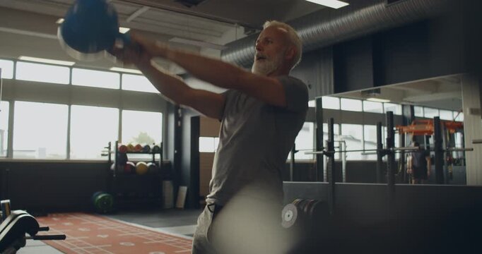 Fit mature man in sportswear
swinging a kettlebell during a workout
session in a gym