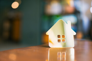 Gold house icon on wooden table with warm blurred background. Concept of home ownership, real...