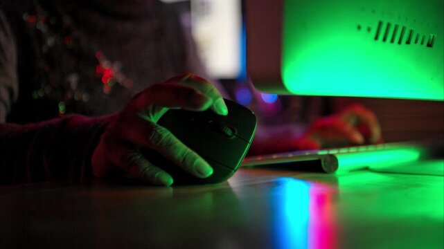Close-up of a person using a gaming mouse with RGB lighting next to a keyboard in a dark room with neon red light