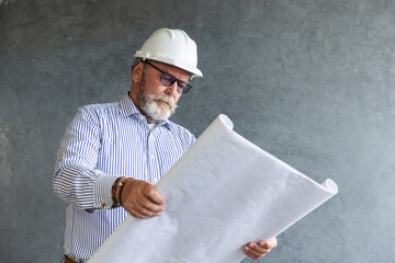 An experienced male engineer wearing a white safety helmet studies construction blueprints, symbolizing architecture, planning, and expertise in building and civil engineering projects.
