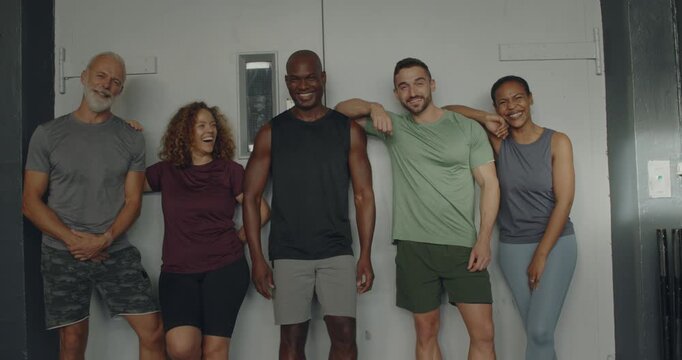 Diverse group of fit people in
sportswear laughing while standing
side by side together after a class in
a gym
