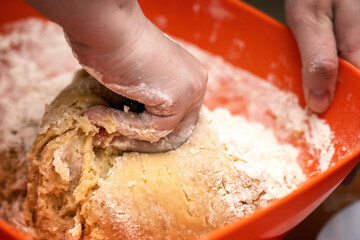 Fototapeta premium Hand kneading honey cookie dough in an orange plastic bowl. Homemade baking process