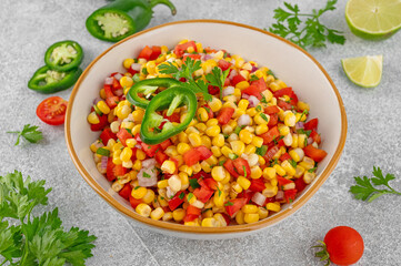 Corn salsa in a bowl with lime, jalapeno pepper, fresh herbs and tortilla chips on a concrete background. Mexican cuisine. Healthy food.