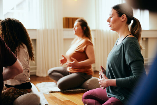People meditating in a restorative yoga class. They are all sitting on a yoga cushion, with their hands in front of them. They are focused and have their eyes closed.