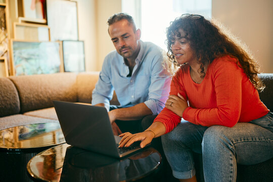 Two People Collaborating on a Project Using a Laptop in Cozy Setting. They are relaxed but focused while looking at the laptop screen.