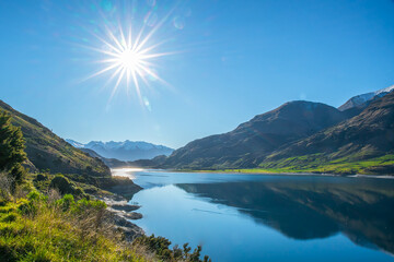 Coastline at Lake Wanaka on a beautiful sunny day with a sun flare in the cloudless sky
