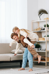 Playful moment of a couple sharing a piggyback ride indoors on a cozy living room setup, sunlight streaming through sheer curtains, creating a warm and joyful atmosphere.
