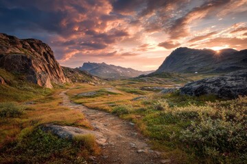 Obraz premium Winding dirt path through a rugged mountain valley under a vibrant sunset sky