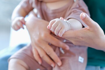 A baby's hand tightly grasps its mother's finger, a mother's love and care for her child.