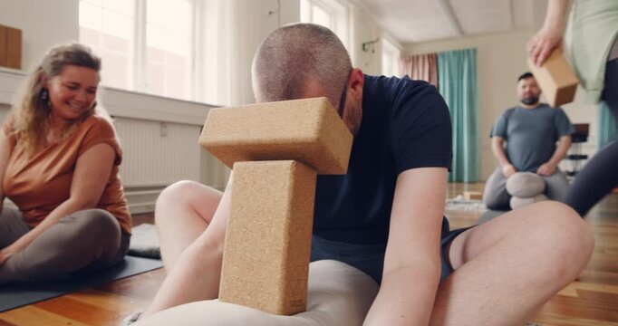 Male yoga student sitting on a studio floor and
using blocks to help with support during a yoga class