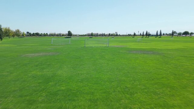 Low drone shot moving backward across soccer goals on green field.