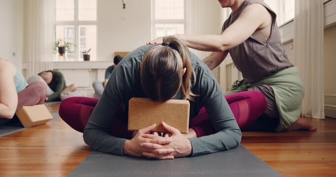 Teacher helping a student in the child's pose
using a block for support during a beginners
yoga class in a studio