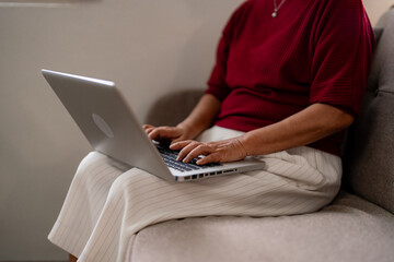 Naklejka premium Older Asian woman remote working from home learning new skills online Senior adult using computer on sofa at apartment Digital literacy for elders