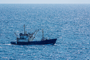Fishing boat in blue sea and clear sky with birds flying overhead.