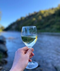 Hand Holding a Glass of White Wine by a River