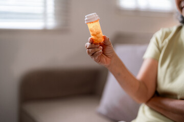Older Asian woman hand hold pill bottle medication health care home wellness senior well being...