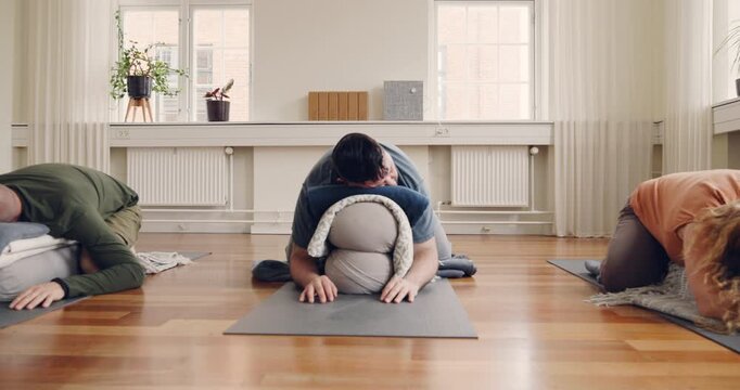 Students using bolster pillows and blocks for
support under the watchful eye of their teacher
during a beginners yoga class