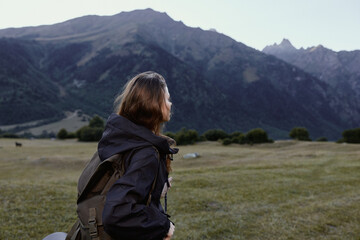Fototapeta premium An outdoor traveler with a backpack gazes toward rugged mountains in a wide valley. She wears weathered gear, breathes fresh air, and savors calm natural scenery.