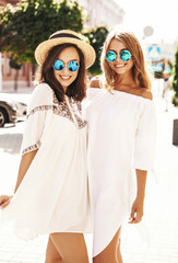 Two young stylish hippie brunette and blond women in summer sunny day. Models dressed in white hipster clothes. Posing on the street background. Going crazy