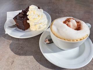 Chocolate cake and cappuccino on white plates in sunlit café