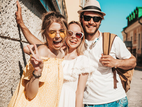 Group of young three stylish friends posing in the street. Fashion man and two cute female dressed in casual summer clothes. Smiling models having fun in sunglasses.Cheerful women and guy outdoors - Powered by Adobe