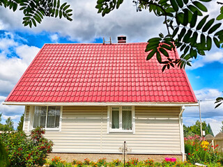 Charming white house with a red roof surrounded by flowers on a sunny day in the countryside