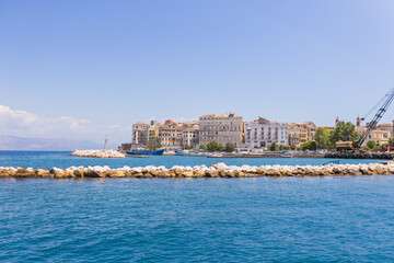 Idyllic, secluded bay in Corfu featuring a stone jetty and a bell tower on a lush green cliff.