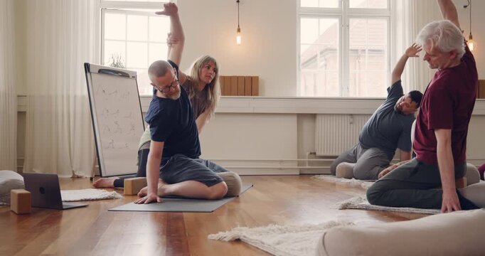 Yoga teacher leading a mixed age range group
of students through the eagle pose during a
beginners yoga class