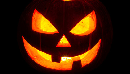 A closeup, frontal view of a carved halloween jackolantern with a menacing expression, illuminated from within