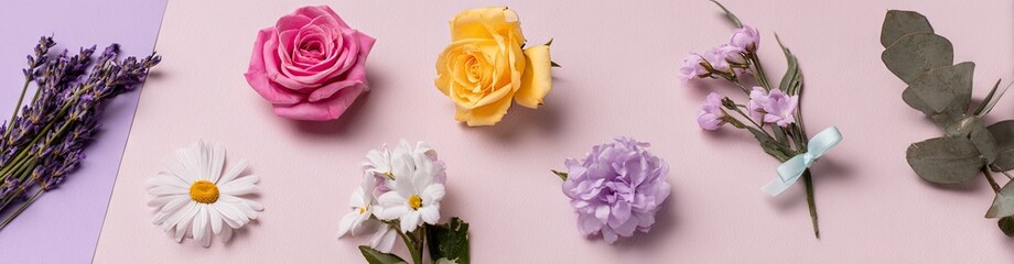 Flat lay arrangement of various flowers on a pastel pink background with a hint of purple