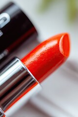 Close-up of a vibrant orange lipstick, next to a black lipstick tube