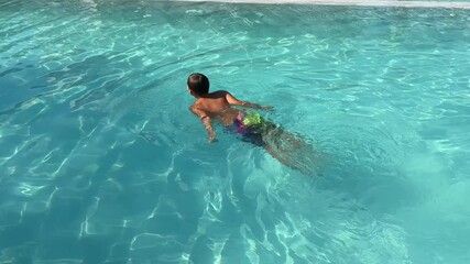 Happy boy swimming in a clear turquoise pool during summer vacation. Active child learning to swim, enjoying water and sunny weather.