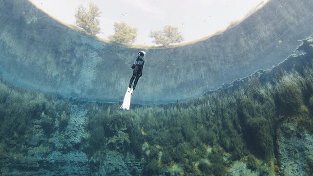 Freediver swims underwater in the crystal clear karst lake with trees reflecting through the water. Woman dives and glides underwater with fins in the blue lake. The lake named Goluboye Ozero, Samara