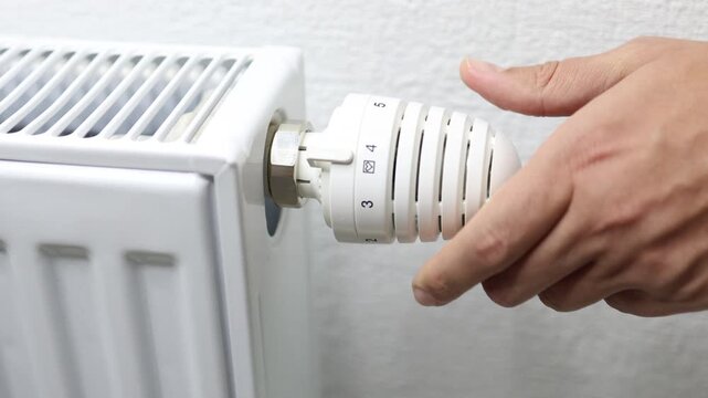 Hand adjusting heating radiator thermostat dial to increase temperature setting, showcasing the transition to winter heating and the importance of warmth in colder seasons