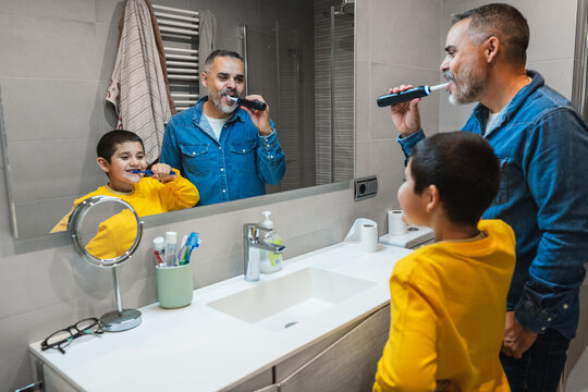 Father teaching son good oral hygiene habits, brushing teeth together in bathroom, promoting family bonding and healthy lifestyle
