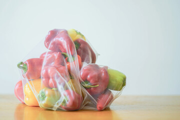 A kilogram of fresh green, yellow, and red bell peppers, packed in a reusable mesh bag on a wooden...