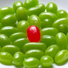 A single vibrant red jelly bean stands out amidst a cluster of green jelly beans, highlighting contrast and individuality.