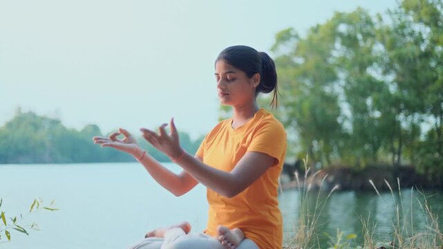 Fit Indian woman sitting in padmasana pose with closed eyes changing gyana mudra to prayer pose in early morning at outdoor.