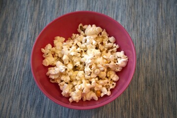 Close-up of fresh popcorn served in a pastel pink bowl against a solid blue background with copy space.