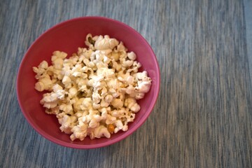 Close-up of fresh popcorn served in a pastel pink bowl against a solid blue background with copy space.
