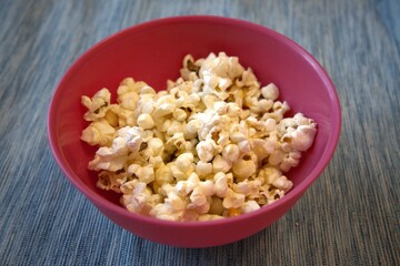 Close-up of fresh popcorn served in a pastel pink bowl against a solid blue background with copy space.