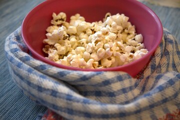 Close-up of popcorn in a pastel pink bowl placed on a blue checkered kitchen towel. Minimal composition with copy space.