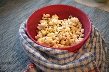 Close-up of popcorn in a pastel pink bowl placed on a blue checkered kitchen towel. Minimal composition with copy space.