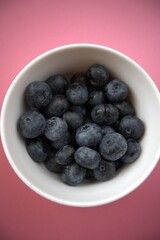 Fresh blueberries in a simple white bowl isolated on a pastel pink background. Close-up food concept with copy space.