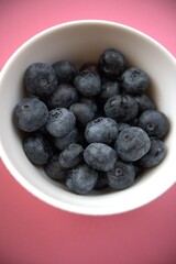 Fresh blueberries in a simple white bowl isolated on a pastel pink background. Close-up food concept with copy space.