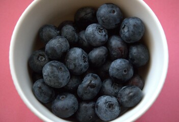 Fresh blueberries in a simple white bowl isolated on a pastel pink background. Close-up food concept with copy space.
