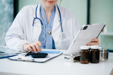 Healthcare costs and fees concept.Hand of smart doctor used a calculator and smartphone, tablet for medical costs at hospital